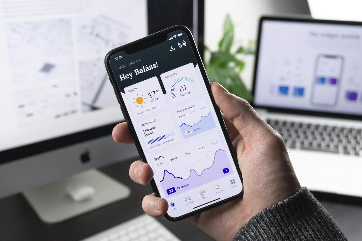 A high-fidelity app screen held on a phone in front of a desktop