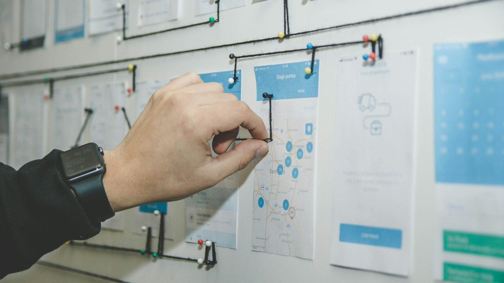 A designer arranging wireframe cards into a user flow on a wall