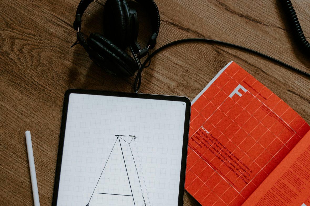 A letterform being drawn on a tablet beside a notebook